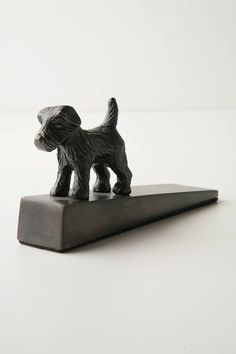 a small black dog figurine sitting on top of a metal stand with white background