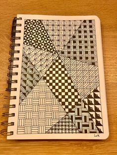 a spiral notebook with black and white designs on the cover, sitting on top of a wooden table