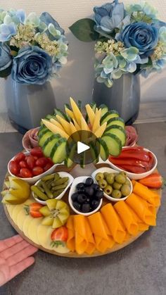 a platter filled with fruits and vegetables on top of a table next to two vases