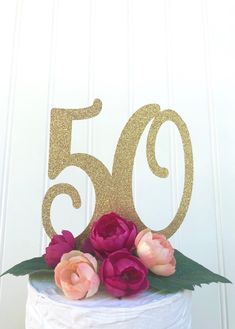 a white cake with pink flowers on top and the number 50 spelled out in gold