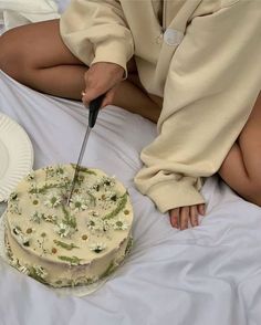 a woman sitting on a bed with a cake and knife in front of her face