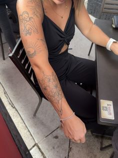 a woman sitting at a table with tattoos on her arm