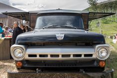 an old pickup truck parked in front of a group of people at a picnic table