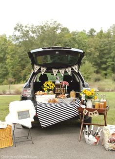 the back end of a car filled with food and drinks, sitting on top of a grass covered field