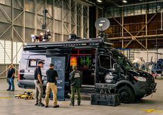 three men are standing in front of a van with an antenna on the roof and one man is looking at it