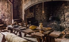 an old stone kitchen with wooden tables and benches in front of the fireplace, surrounded by brick walls