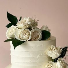 there is a white cake with flowers on the top and bottom tier, along with greenery