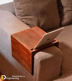 a laptop computer sitting on top of a wooden stand in front of a gray couch