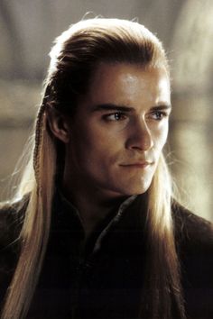 a man with long blonde hair wearing a black shirt and braided ponytail is looking at the camera