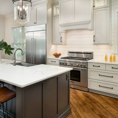 a kitchen with an island, stove and sink in the center is surrounded by white cabinetry