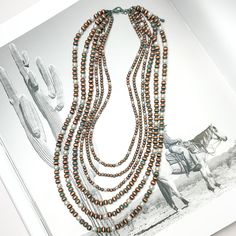 Six Strand Faux Navajo Pearl Necklace in Patina Tone with White Pearl Beads. Pictured on a western background. Navajo Pearls Necklace Outfit, Southwestern Multi-strand Beaded Necklace With Large Beads, Layered Navajo Pearls, Southwestern Multi-strand Necklaces With Large Beads, Southwestern Multi-strand Polished Beaded Necklaces, Giddy Up Glamour, Navajo Jewelry, Layering Pieces, White Pearl