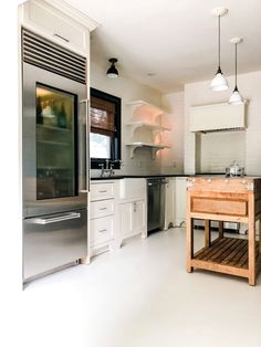 a modern kitchen with stainless steel appliances and wood island in the foreground, white cabinets on both sides