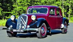 an old fashioned car is parked on the side of the road in front of some trees