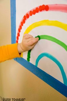 a child's hand is on the side of a rainbow wall hanging with beads