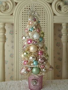 a small christmas tree with ornaments in a pink pot on a white doily covered table