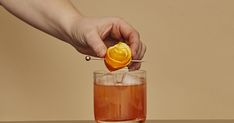 a person is squeezing an orange into a cocktail in a tall glass with a straw