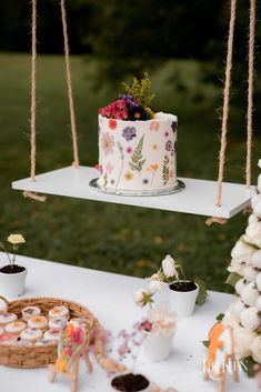 a cake and cupcakes sitting on a table with flowers in the air above it