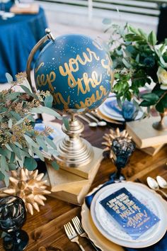 a table topped with plates covered in blue and gold foiled decorations next to a vase filled with flowers