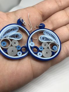 a pair of blue and white earrings in the palm of a person's hand