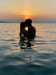 a couple kissing in the water at sunset on a lake or ocean with their backs to each other