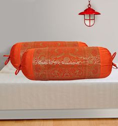 two orange pillows sitting on top of a bed next to a red light hanging from the ceiling