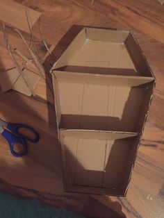 an open cardboard box sitting on top of a wooden floor next to scissors and paper