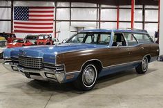 an old station wagon is parked in a garage with other classic cars and american flags