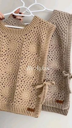 two crocheted sweaters hanging on a white hanger, one is brown and the other is beige