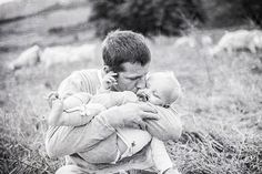 a black and white photo of a man holding a baby while sheep graze in the background