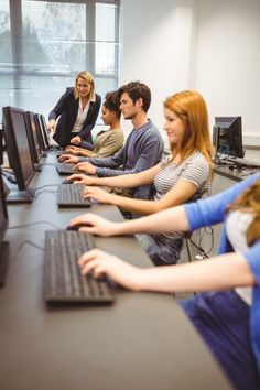 a group of people sitting in front of computer monitors with their hands on the keyboard