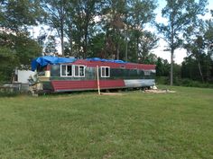 a red and black trailer sitting in the middle of a field next to some trees