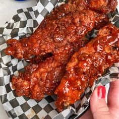 two pieces of chicken wings covered in bbq sauce on a checkered paper plate