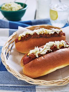 two hot dogs in buns with toppings sit on a plate next to a bowl of coleslaw