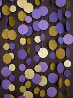 purple, gold and white paper circles hanging from strings on a black wall with string