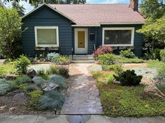 a blue house with landscaping in front of it and trees on the other side of the house