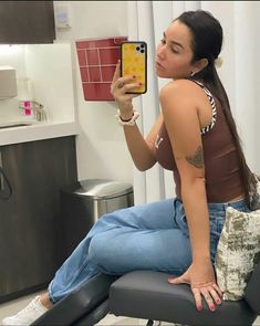 a woman taking a selfie with her cell phone in the bathroom while sitting on a chair