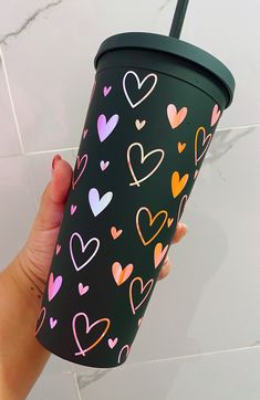 a hand holding a black cup with hearts on it