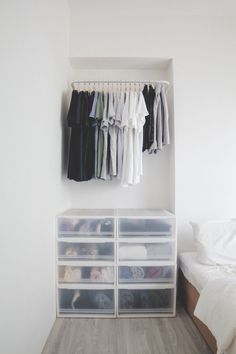 a white closet with clear drawers and clothes hanging on the wall next to a bed