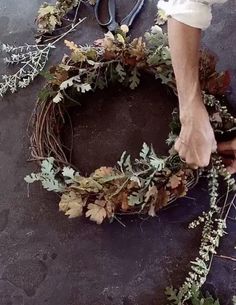 someone is making a wreath out of branches and leaves on the ground with their hands