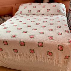 a white bed with pink roses on it in a room next to a wall and window