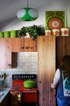 a woman standing in a kitchen next to a stove top oven and green potted plant