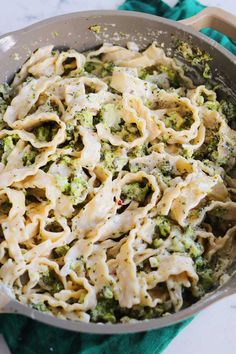 a skillet filled with pasta and broccoli on top of a green towel