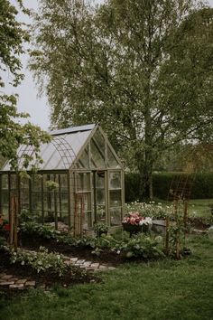 a small greenhouse in the middle of a garden with lots of plants and flowers around it