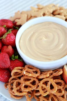 a white plate topped with pretzels, strawberries and cookies next to a bowl of peanut butter