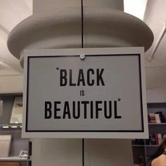 a sign that says black is beautiful hanging from a ceiling in an office building with people standing around