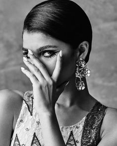 a black and white photo of a woman covering her face with her hands while wearing earrings