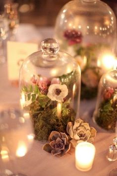 several glass domes with flowers and candles on a table