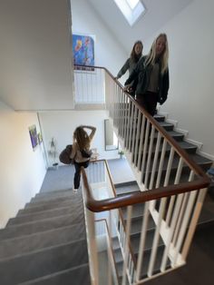 two women walking up the stairs in a house with white walls and wood handrails