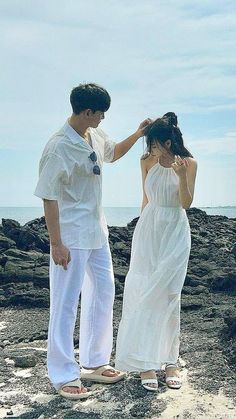 a man and woman standing on top of a rock covered beach next to the ocean