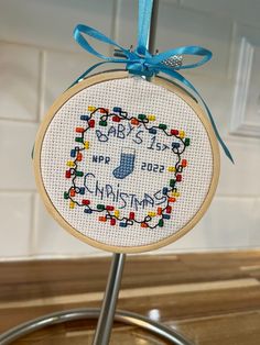 a cross - stitch christmas ornament hanging on a kitchen counter with blue ribbon